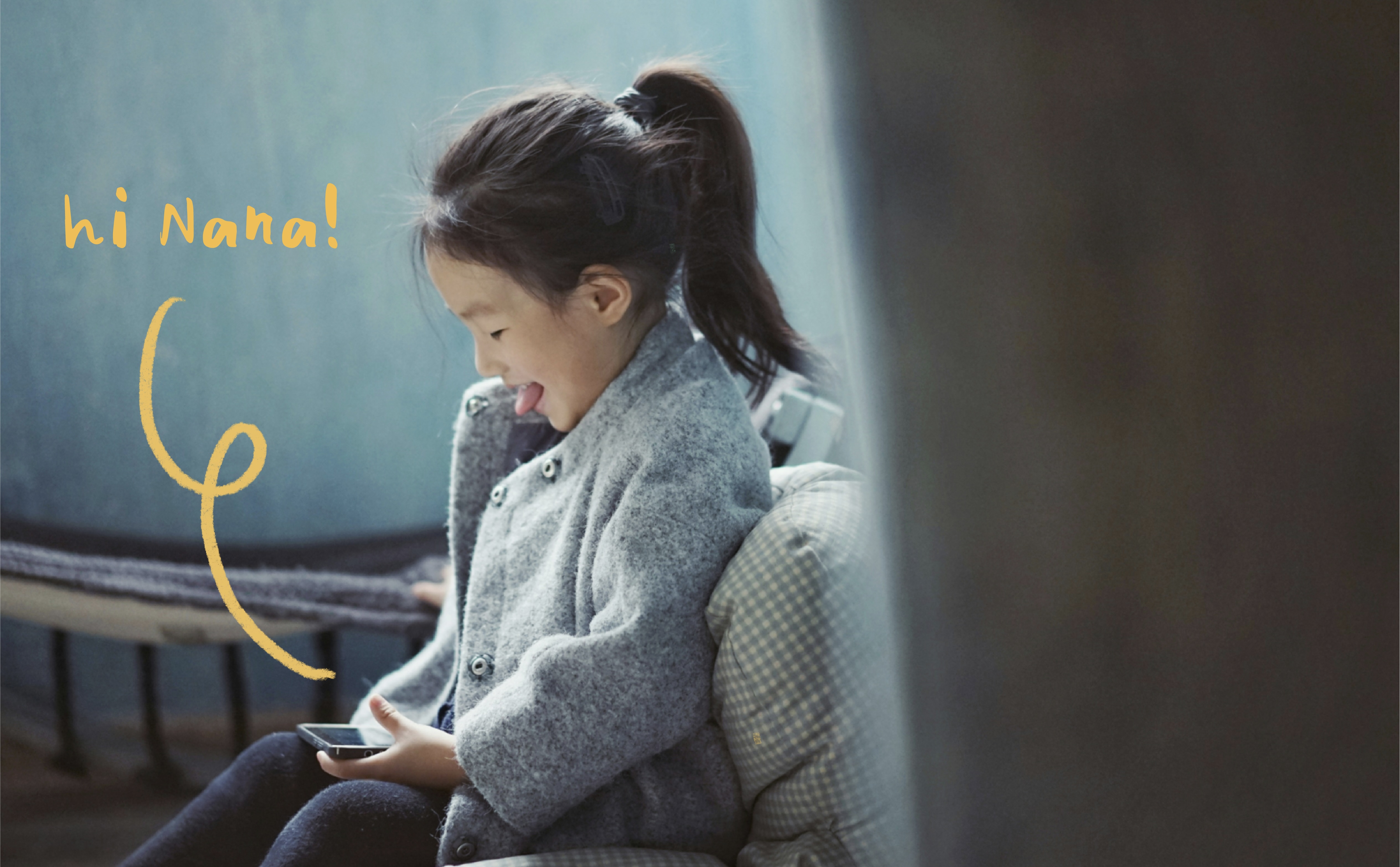 Image of a little girl smiling and looking down at a phone in her lap. A squiggle is drawn up from the phone and leads to text that says, "Hi Nana!"